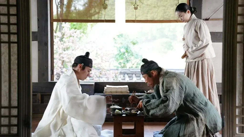 한옥 실내에서 흰 옷을 입은 젊은 왕과 회색 옷차림의 엄흥도가 작은 상을 사이에 두고 마주 앉아 식사하고, 뒤편에서는 여성이 조용히 시중드는 한국 사극 영화의 한 장면.