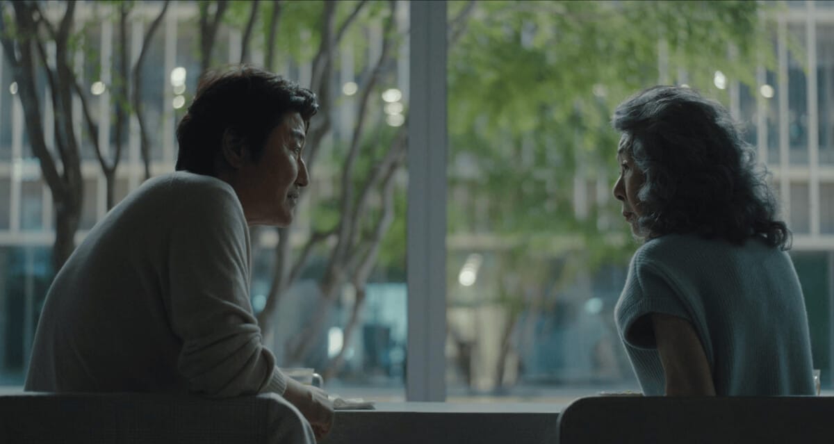큰 창 너머 초록빛 풍경을 배경으로 중년 남성과 노년 여성이 마주 앉아 조용히 대화하는 넷플릭스 시리즈 성난 사람들의 장면.