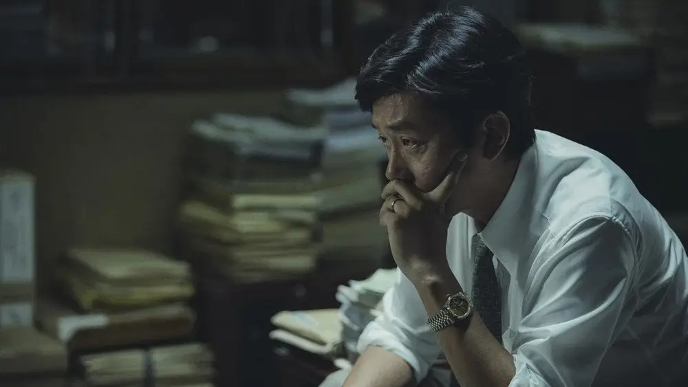 1987 영화 스틸 이미지로, 최환역을 연기하는 하정우배우가 어두운 사무실에서 손으로 입을 가린 채 깊은 고민에 잠긴 모습