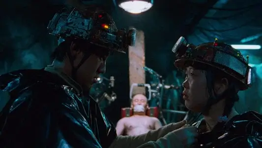 영화 지구를 지켜라 속 두 인물이 특수 헬멧과 우비를 입고 마주 서 있고 뒤편에 결박된 남성이 보이는 장면으로, 기묘한 동맹과 납치 상황의 긴장을 담은 스틸 이미지