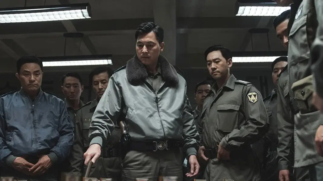 서울의 봄 영화 스틸 이미지로, 군 지휘관이 중앙에 서서 다수의 장교들에게 둘러싸인 채 작전 현장을 통제하는 쿠데타 긴장 장면