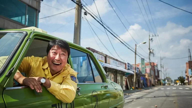 택시운전사 영화 스틸 이미지로, 김만섭역을 연기하는 송강호배우가 녹색 택시 창문 밖으로 몸을 내밀고 환하게 웃는 모습이 담긴 장면