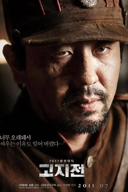 고지전 영화 포스터 이미지로, 군모를 쓴 병사의 얼굴 클로즈업을 중심으로 전쟁의 피로와 냉혹한 감정을 강조한 한국 전쟁 영화 비주얼