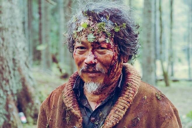 낙연 역을 연기하는 이상희 배우가 얼굴에 피와 흙이 묻은 채 숲속을 바라보는 영화 호프 장면.